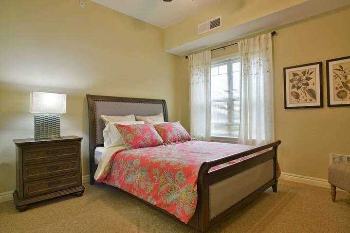 A cozy bedroom featuring a well-made bed with floral bedding, complemented by warm lighting and elegant curtains.