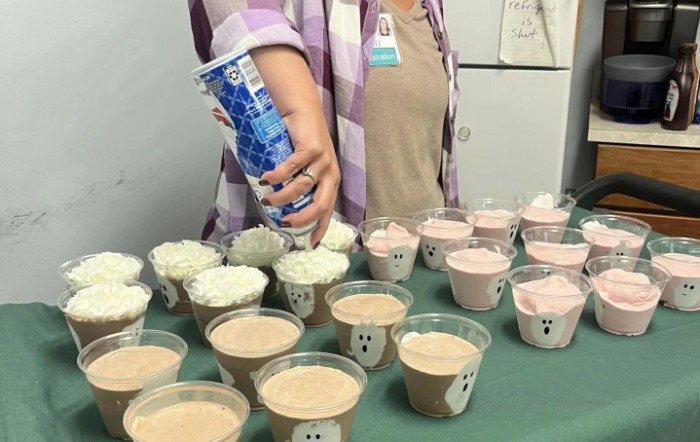 Person decorating pudding cups with whipped cream for a Halloween-themed dessert.