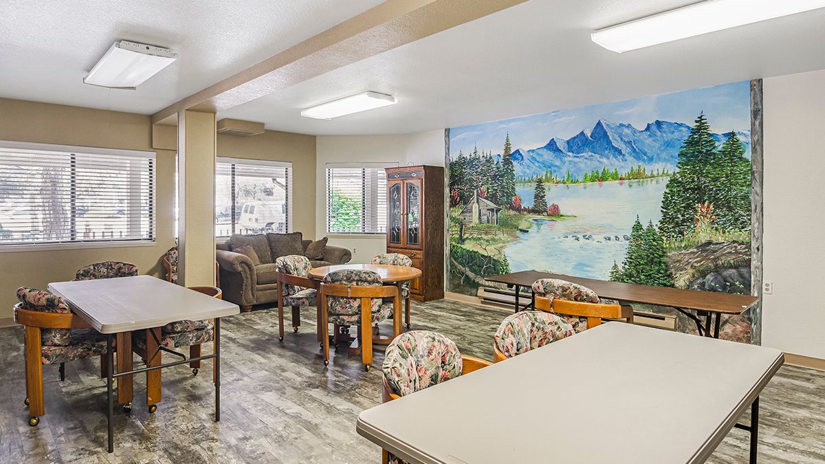 A community room with a mural depicting a scenic landscape, furnished with tables, chairs, and sofas.
