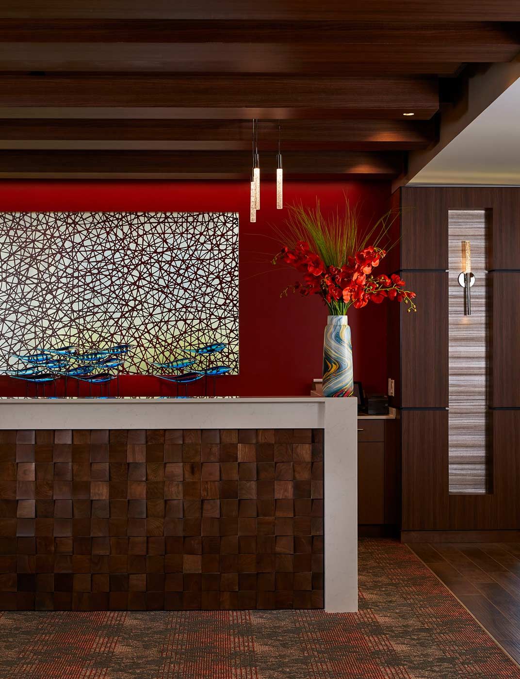 A modern reception area featuring a colorful artwork, a vase with red flowers, and sleek wooden textures.