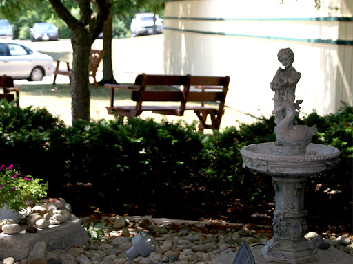 A serene garden scene featuring a bench surrounded by lush greenery and a decorative fountain with a statue.