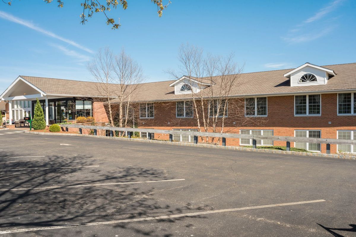 A brick building with a large parking lot in front, surrounded by trees under a clear blue sky.