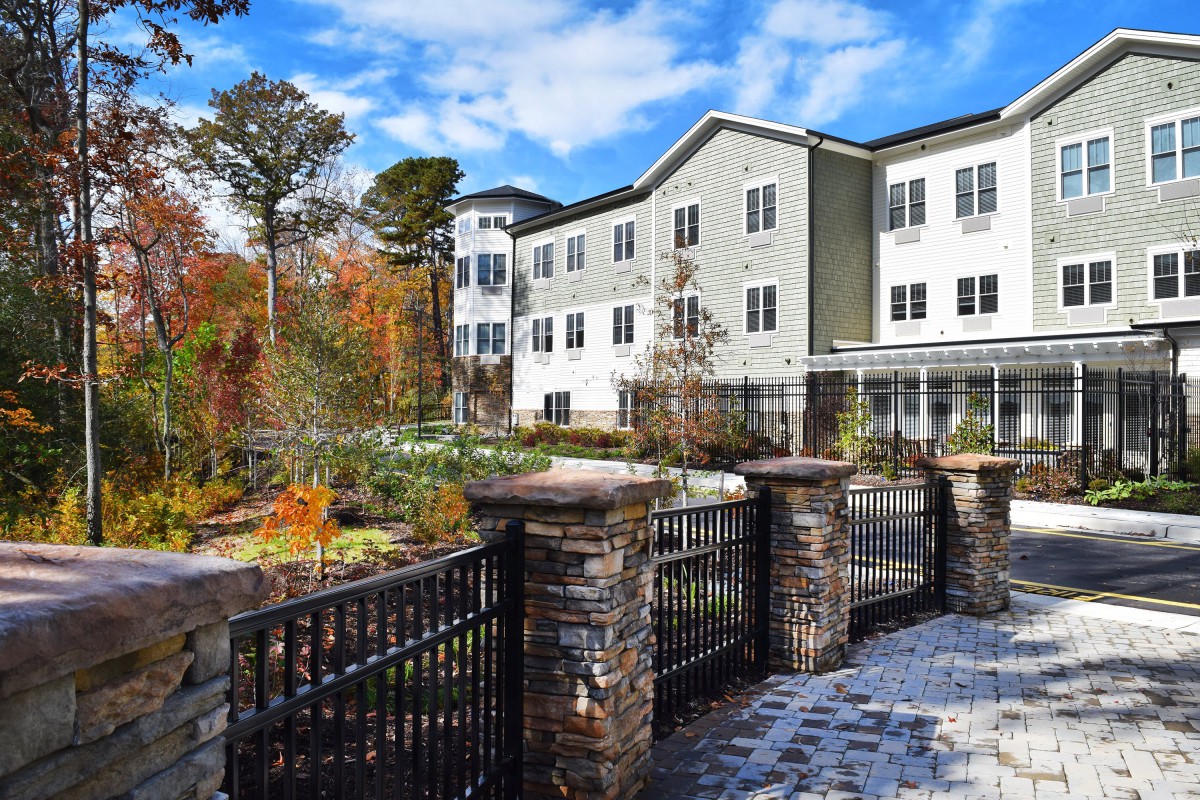 A residential building with a garden and fence surrounded by autumn trees.
