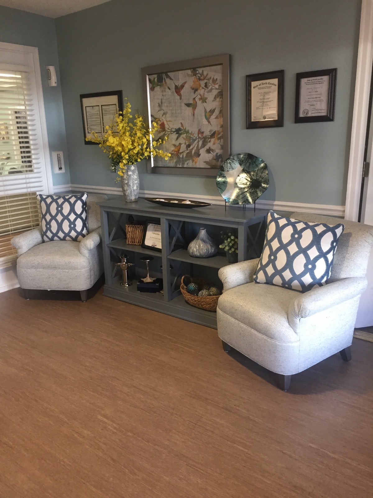 A cozy lounge area featuring two armchairs, a decorative cabinet with flowers, and framed artwork on the wall.