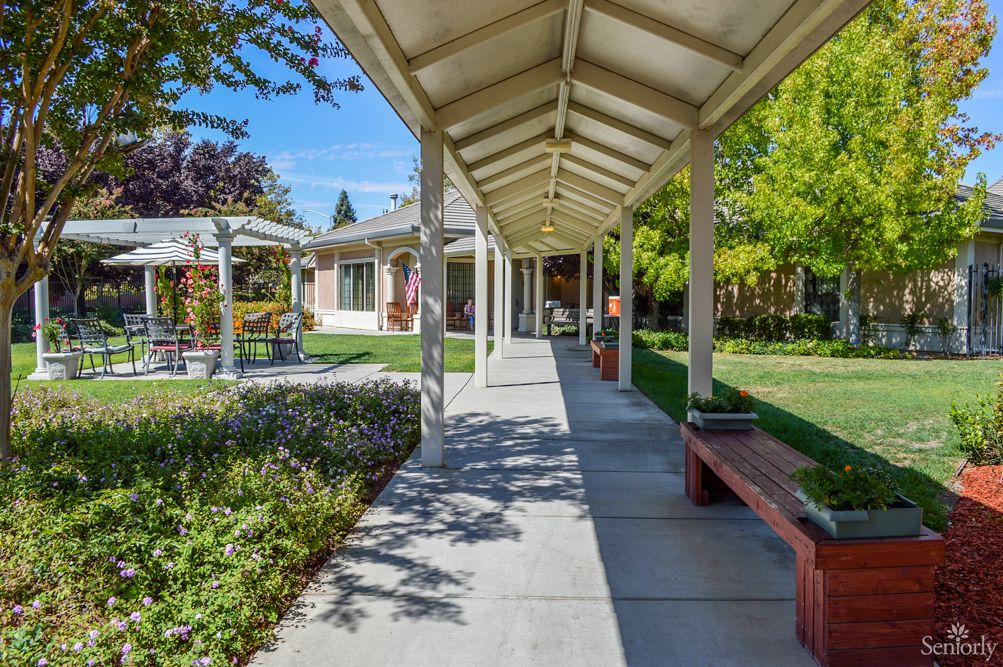 A covered walkway surrounded by a garden with benches on a sunny day.