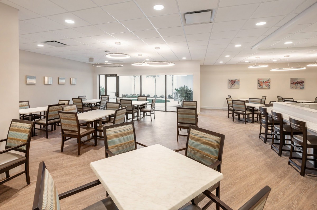 A modern dining area with neatly arranged tables and chairs, featuring bright lighting and wooden flooring.