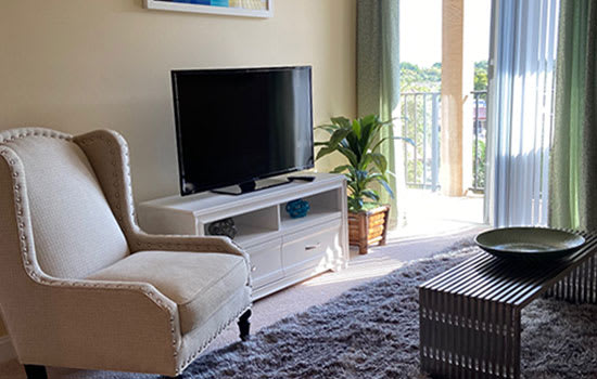 A cozy living room with a TV, armchair, and a view of the balcony.