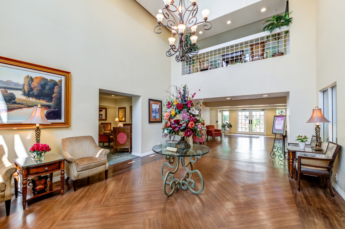 A spacious and elegantly decorated lobby featuring a chandelier, floral centerpiece, and artwork.