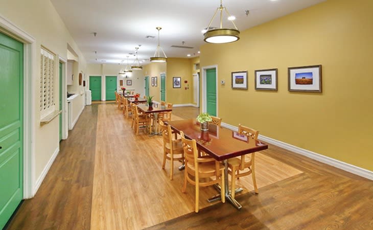 A bright dining area with wooden tables and chairs, featuring wood flooring and wall decorations.
