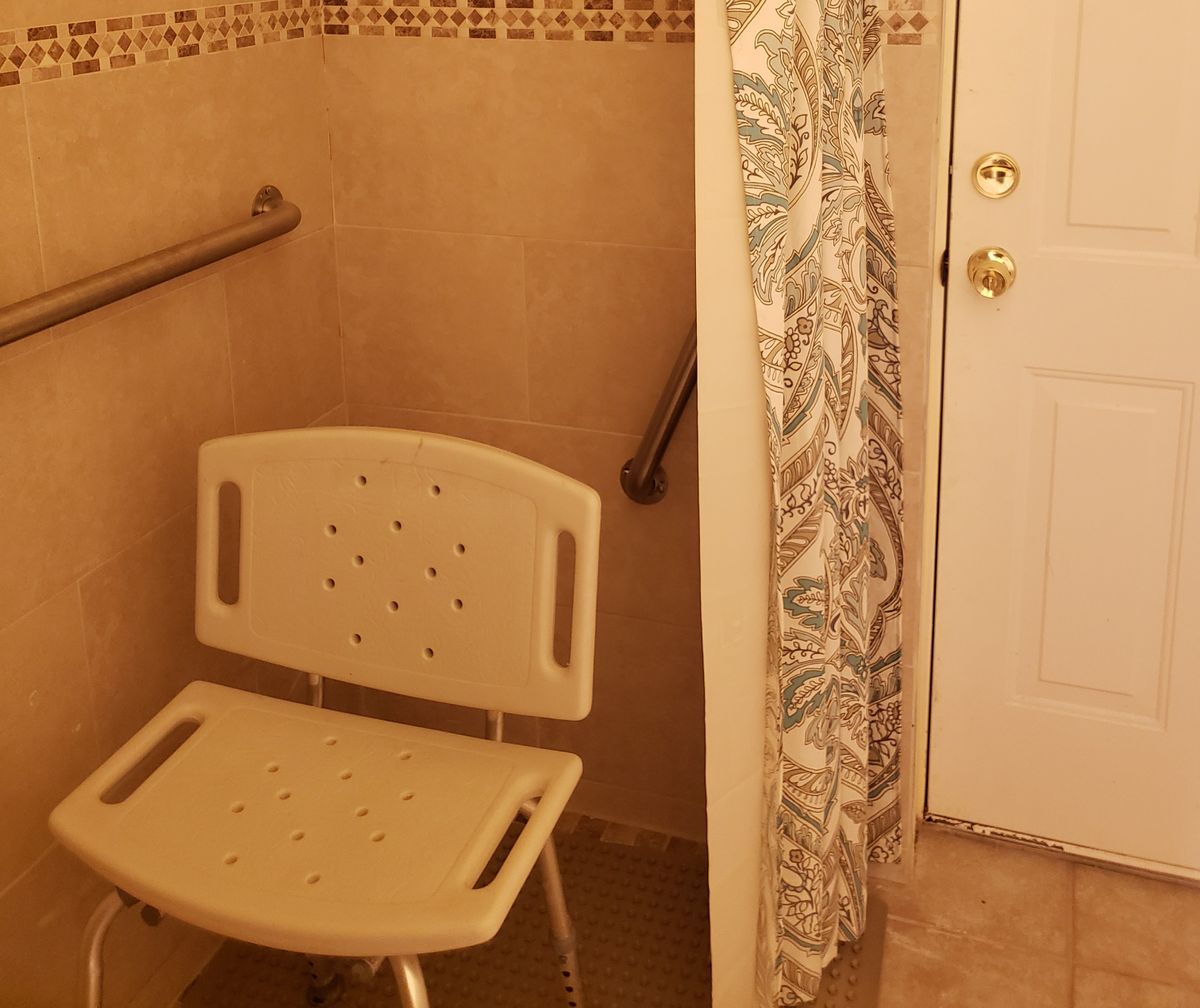 An accessible bathroom with a shower chair and grab bars.