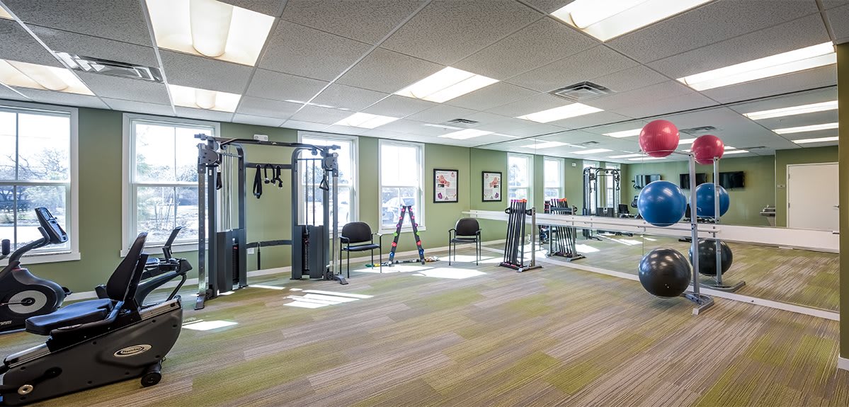 A well-lit gym with fitness equipment and mirrors lining the walls.