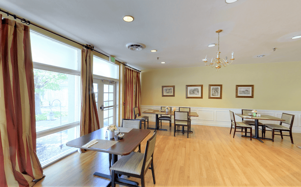 A cozy dining room with wooden floors, tables, and framed artwork on the walls.