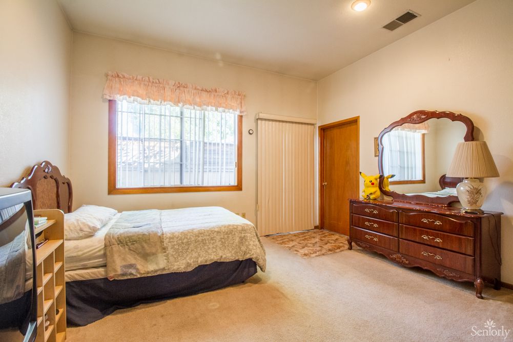 A cozy bedroom with a bed, wooden dresser, and a curtained window.