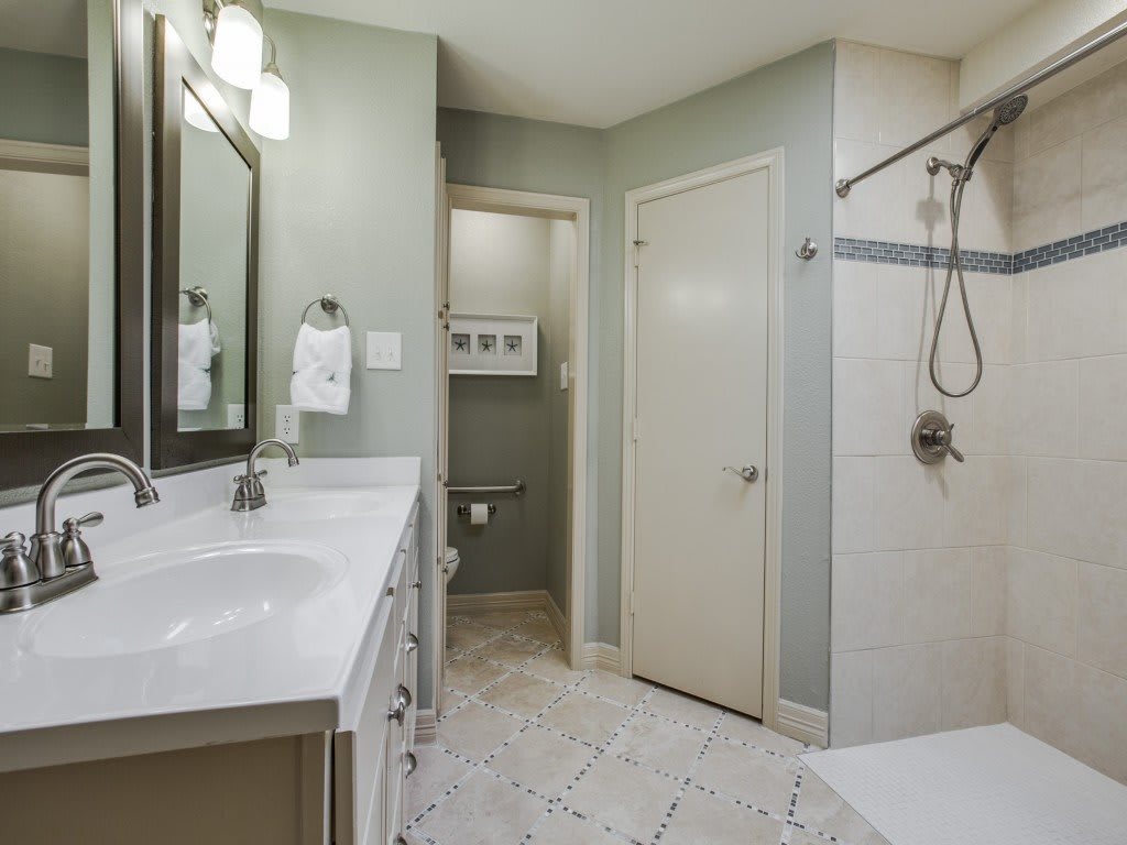 A modern bathroom with a sleek design featuring a large mirror, double sinks, and a walk-in shower.