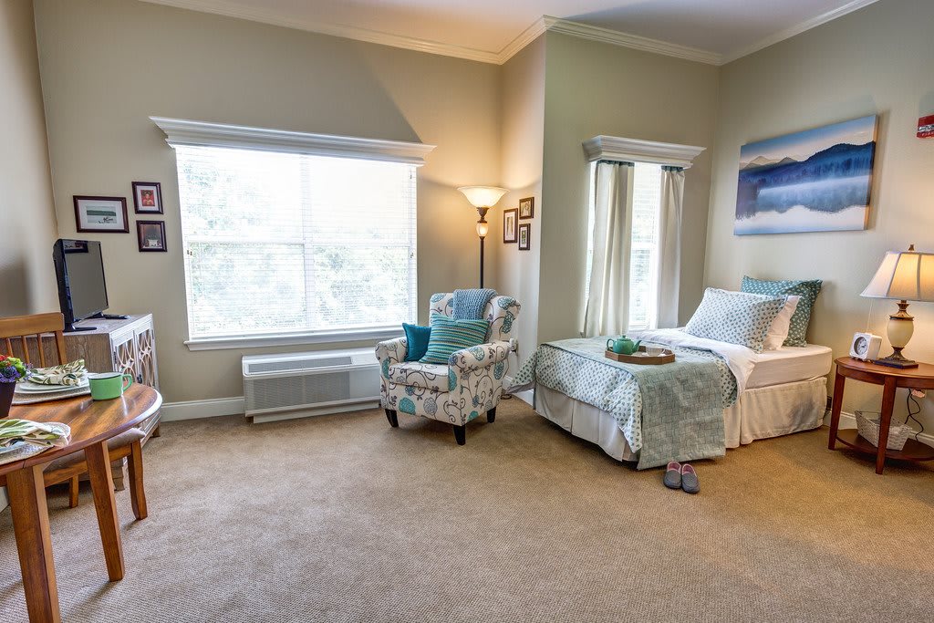 A cozy bedroom with a bed, armchair, and large window creating a bright and welcoming atmosphere.