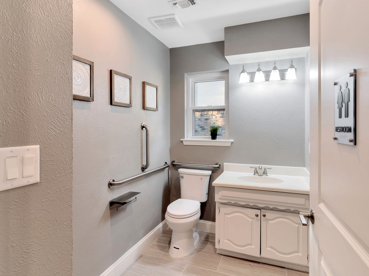 A modern bathroom with a toilet and sink, featuring a light fixture above the mirror.