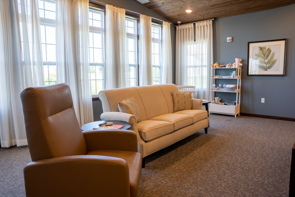 A cozy living room with a beige sofa and armchair, bathed in natural light from the large windows.