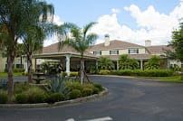 A scenic view of a building surrounded by lush greenery and palm trees, set against a cloudy sky.