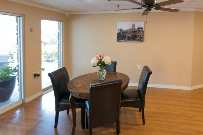 A cozy dining room with a wooden table surrounded by four chairs, adorned with flowers in a vase.