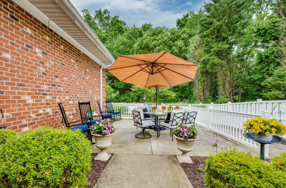 A cozy patio with garden furniture and an umbrella, surrounded by greenery.