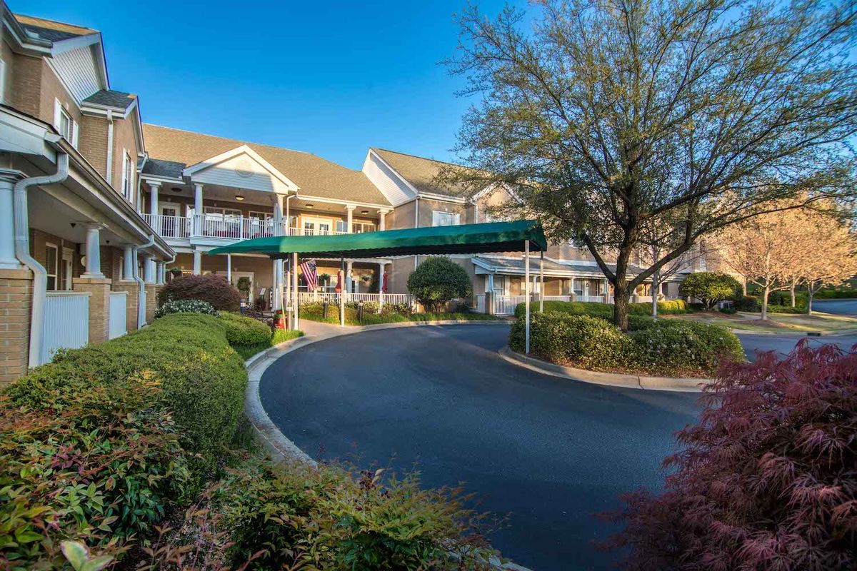 A picturesque retirement home with a circular driveway surrounded by well-maintained gardens and large trees.