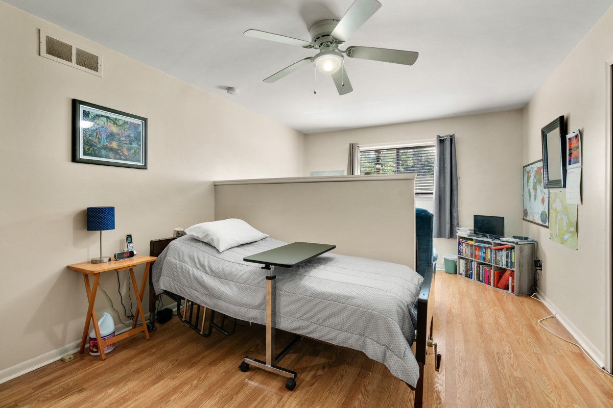 A neatly arranged bedroom with a single bed, wooden flooring, and a ceiling fan.