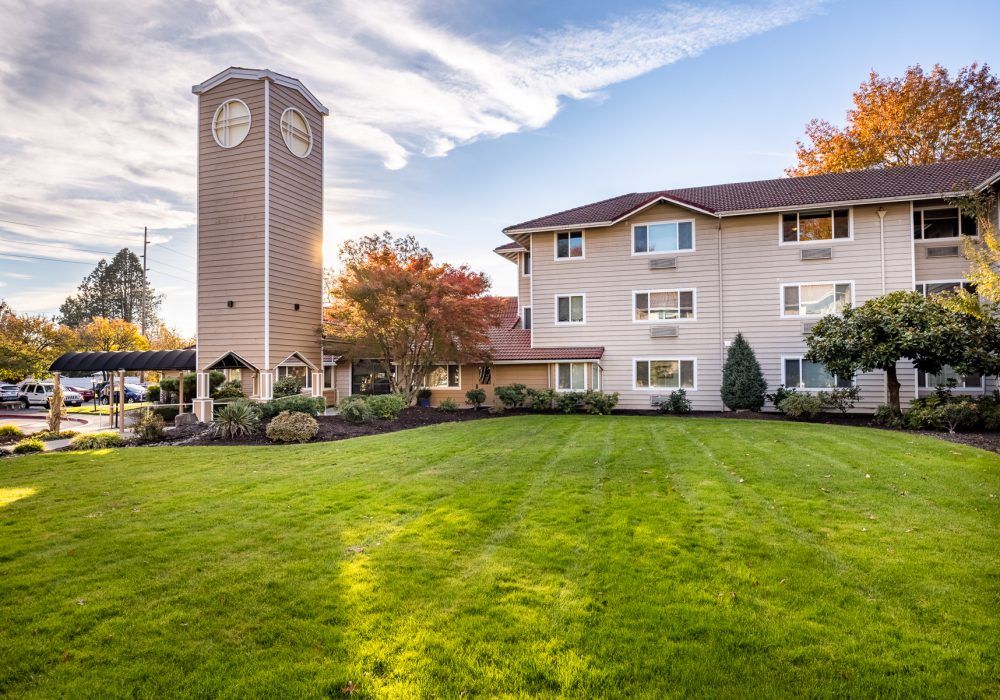 A scenic view of a building with a clock tower, surrounded by a well-maintained lawn and trees under a partly cloudy sky.