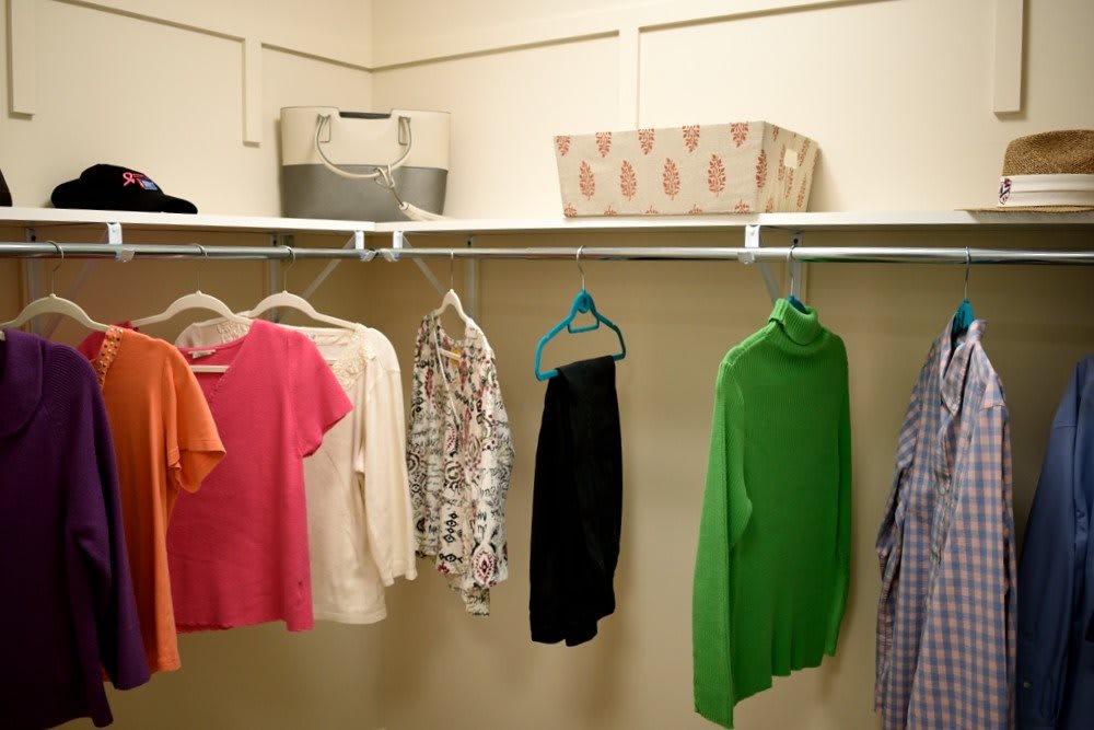 A neatly organized closet with colorful clothing on hangers and storage boxes on the shelf.