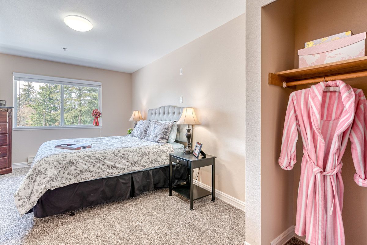 A cozy bedroom with a large bed, side tables with lamps, and an open closet displaying a pink robe.