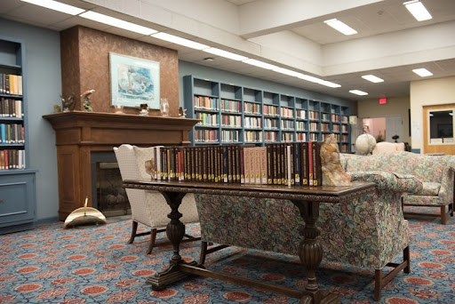 A cozy library setting featuring a table, comfortable chairs, and a well-stocked bookshelf.