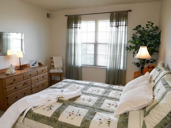 A cozy bedroom with a neatly made bed, quilt, dresser, and soft lighting.