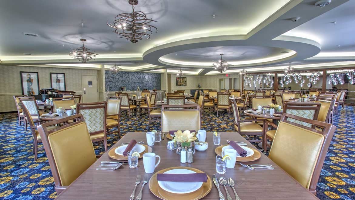 An elegantly set dining room with multiple tables, chairs, and chandeliers.