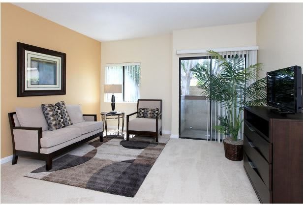 A cozy living room with modern furniture, a potted plant, and a sliding glass door leading to an outdoor area.