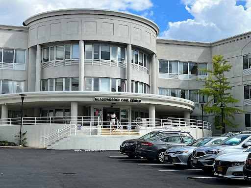 A modern architectural building with a parking lot in front under a blue sky.