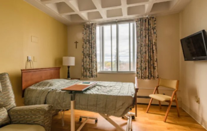 A hospital room with a bed, window, and simple furnishings.