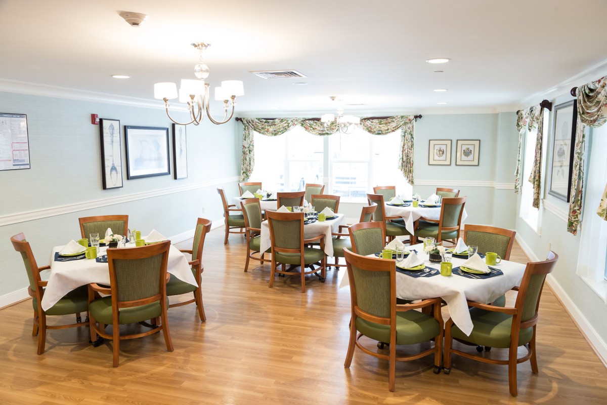 An elegant dining room with neatly arranged tables and chairs, featuring a chandelier and wooden flooring.