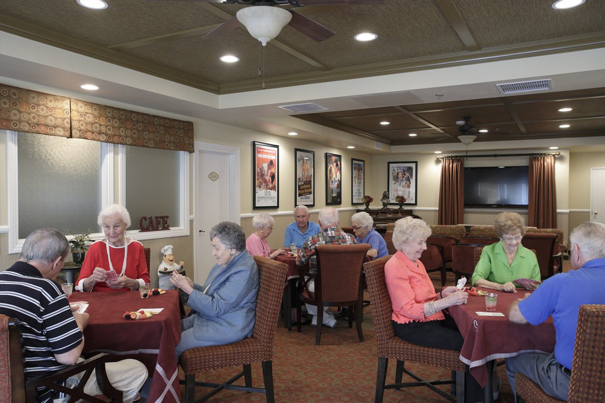 A group of seniors sitting around tables, engaging in social activities inside a community room.