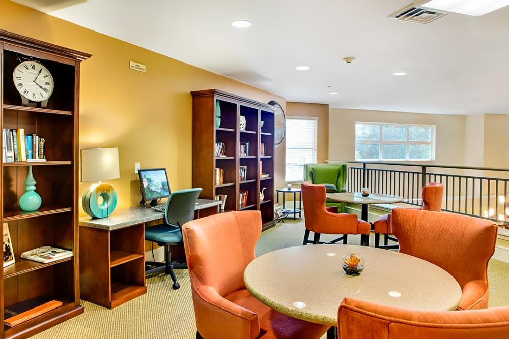A brightly lit lounge area with comfortable seating, a computer station, and a bookshelf.