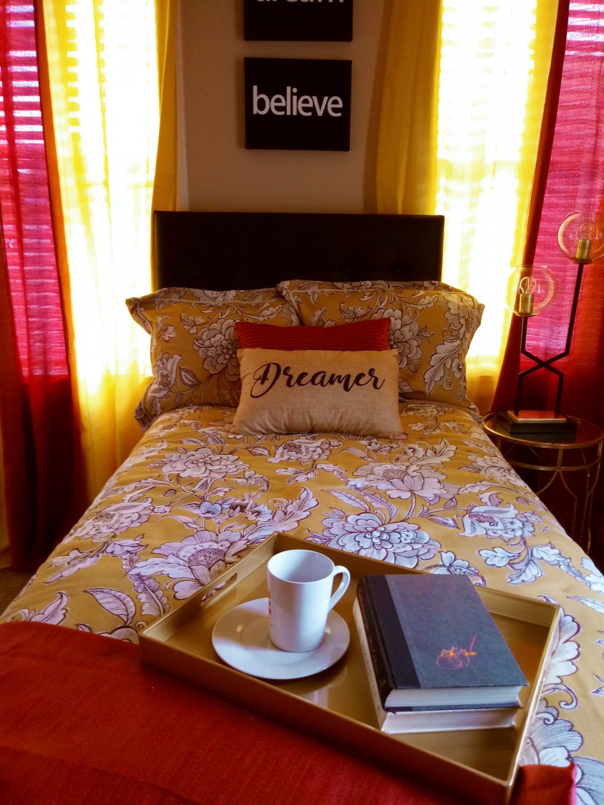 A cozy bedroom with colorful bedding, decorative pillows, and a tray with a book and cup on the bed.