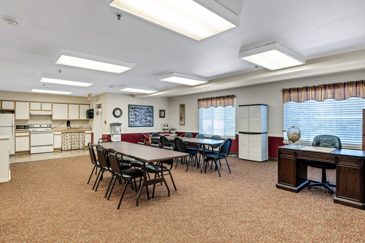 A spacious meeting room equipped with tables and chairs, featuring a whiteboard and natural lighting from multiple windows.
