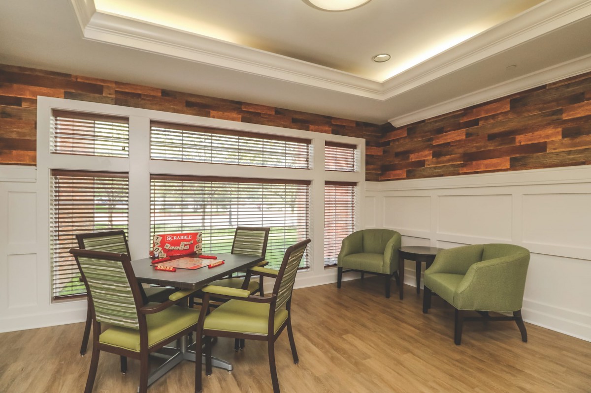 A cozy dining area with green chairs, a wooden floor, and large windows letting in natural light.