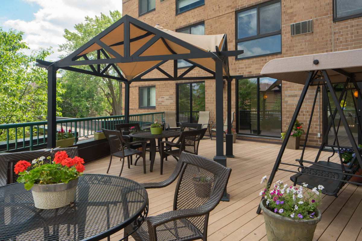 A well-furnished outdoor patio with a gazebo, tables, and chairs on a deck beside a building.