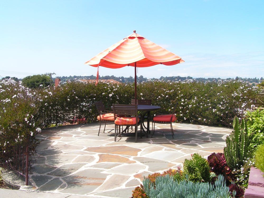 A sunny patio with an orange umbrella, surrounded by a lush garden.