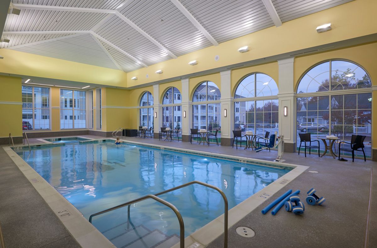 A well-lit indoor swimming pool area featuring large arched windows and seating arrangements.