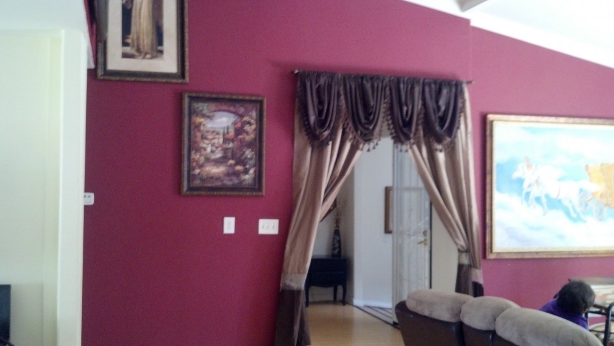A cozy living room interior with a red accent wall, decorative curtains, and framed artwork.