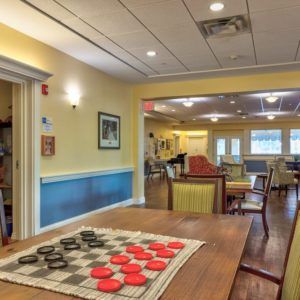 A cozy recreation room featuring a checkers board on a table, surrounded by chairs and warm lighting.