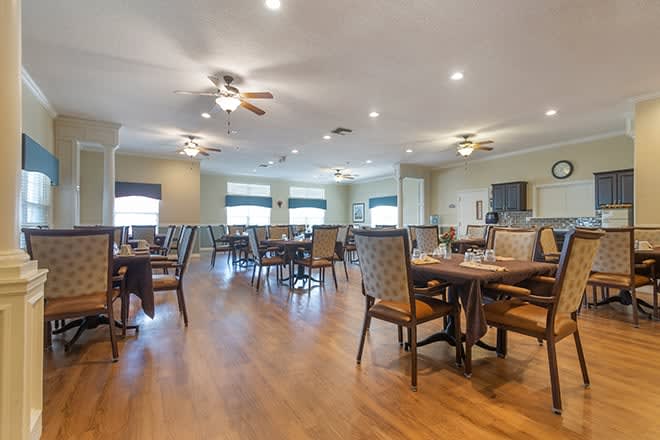 A spacious and well-lit dining area with multiple tables and chairs, featuring ceiling fans and wooden flooring.