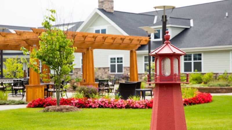A beautifully landscaped garden featuring a pergola, colorful flowers, and outdoor seating in front of a charming house.
