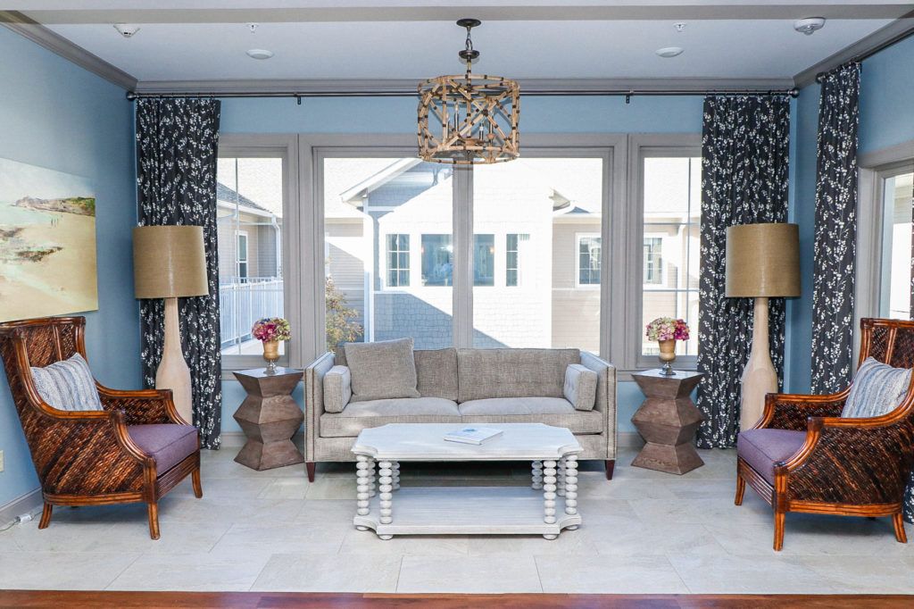A well-decorated living room with a sofa, coffee table, and chandelier surrounded by large windows.