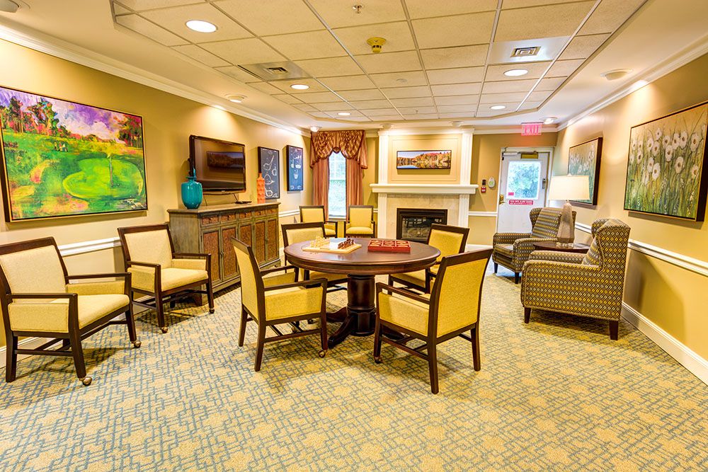 A cozy living room with a round table surrounded by chairs, warm lighting, and colorful artwork on the walls.